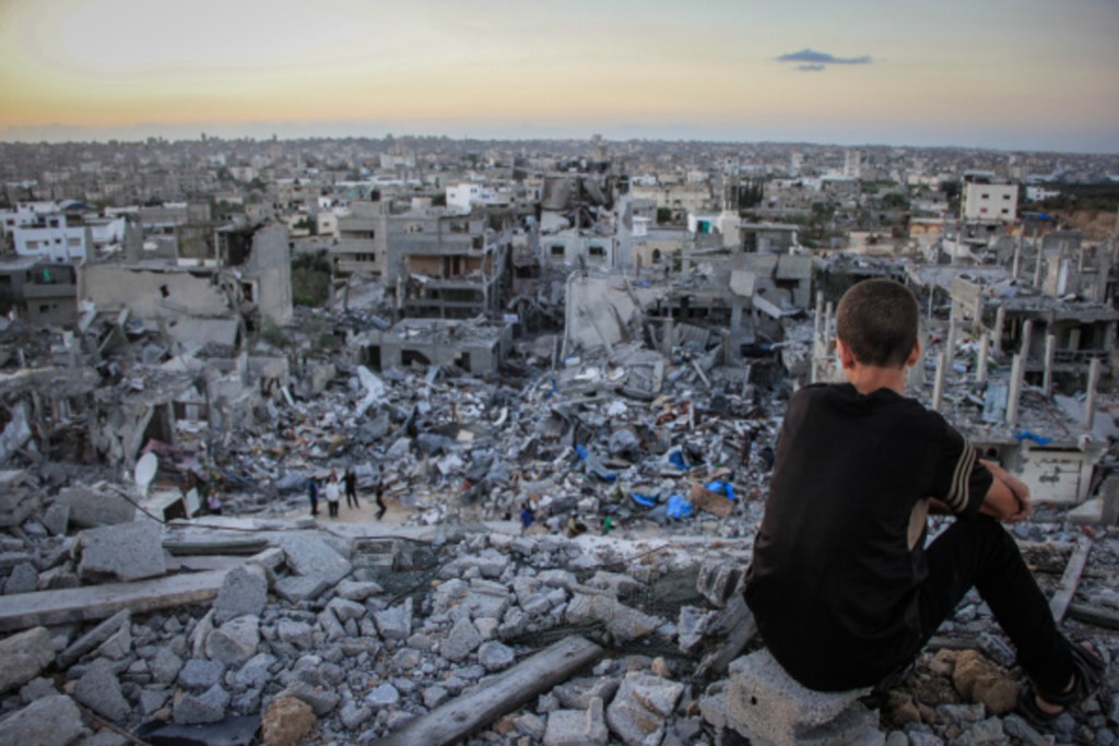 A Palestinian child sits above the ruins of his ruined home, and looks at thousands of homes destroyed because of the war on Gaza.